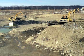 Two Crews Work to Remove Waste Material from Pit 2.
The Waste Pits Remedial Action Project (WPRAP) involves the remediation of six waste pits, the Burn Pit, the Clearwell, miscellaneous structures, facilities, and soil. More than 1 million tons of contaminated materials are associated with the cleanup project. The Shaw Group, formerly IT Corporation, constructed the remediation facilities for the project, which include a Material Handling Building, where excavated wastes from the pit area will be sorted, blended and treated, Gas Control System/ Water Treatment System (GCS/WTS) Building, and the Railcar Loadout Building, where material is loaded into railcars for shipment to Envirocare of Utah.
Keywords: Fernald Closure Project Fernald Green Salt Plant, Feed Materials Production Center, Fernald, Ohio (FEMP)