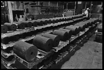 Ingots of Fernald at Ashtabula
These ingots, made at Fernald by remelting uranium metal derbies, have been trucked 300 miles northeast to Ashtabula, Ohio, for further processing. Here they will be submerged in molten salt until they reach a red-hot 1100F. Then thy will be inserted into the Ashtabula uranium metal extrusion press. The sign in the background reads "Caution: Radioactive Materials." 

Reactive Metals, Incorporated, Ashtabula, Ohio. June 19,1984.
Keywords: Fernald Ashtabula