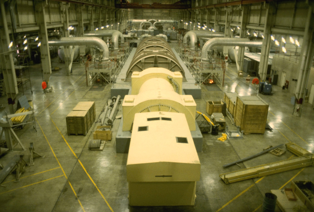 Interior of the turbine building at the Donald C. Cook Nuclear Generating Station. In the foreground is the Unit 1 electrical generator (yellow), followed by the Unit 1 low pressure turbines (brown). In the background are the Unit 2 turbine and generator. The large silver pipes contain the steam going to the various parts of the turbine.
